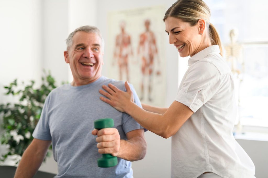 Una fisioterapeuta riéndose junto a un paciente realizando ejercicio.